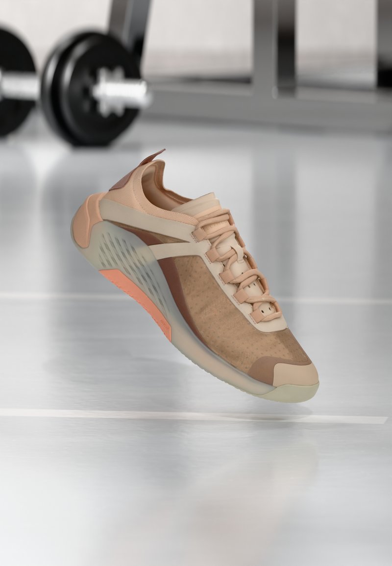 Scarpa sportiva color sabbia con tomaia in mesh e dettagli in gomma. Presenta pannelli testurizzati, chiusura con lacci e suola traslucida con dettaglio arancione.