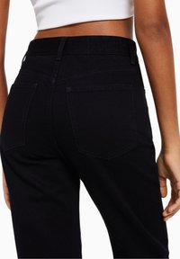 Mustat korkeavyötäröiset farkut, valmistettu deniimistä, joissa on sileä rakenne, kaksi takataskua ja hienovaraisia ompeluyksityiskohtia.