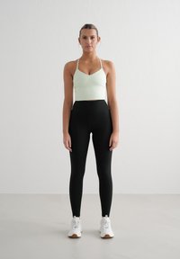 Top corto a costine verde chiaro con spalline sottili, abbinato a leggings neri a vita alta. Scarpa da ginnastica bianca completa l'outfit.
