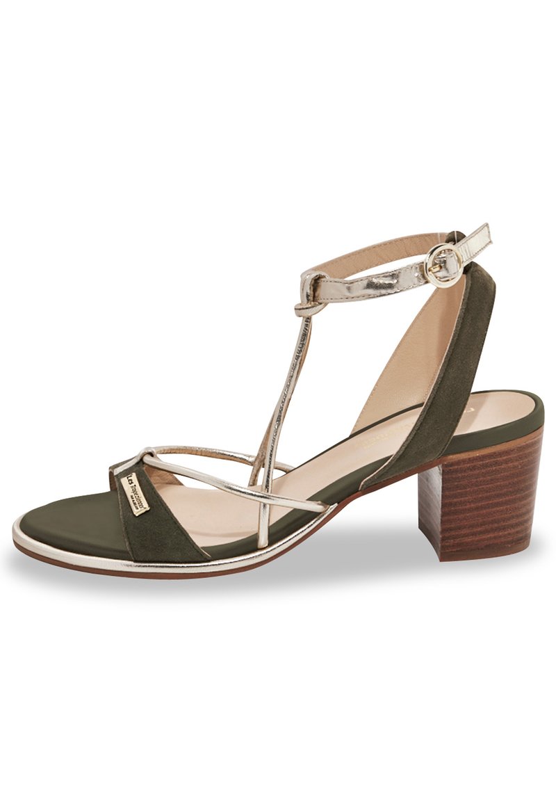 Sandalo con tacco in suede verde oliva con accenti metallici. Presenta una punta quadrata, cinturini incrociati e un tacco a blocco con texture legnosa.