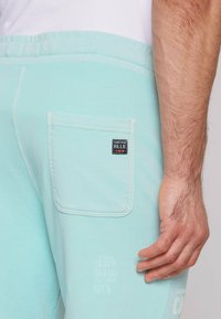 Lichtblauwe joggingsbroek van katoen, met een zijzak en een label met de tekst "CAMP DAVID BLUE CREW", en subtiele witte tekstdetails.