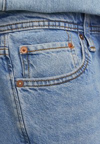 Lichtblauwe denim jeans met een klein voorvak en koperen hardware. Duidelijke stikdetails accentueren het ontwerp.