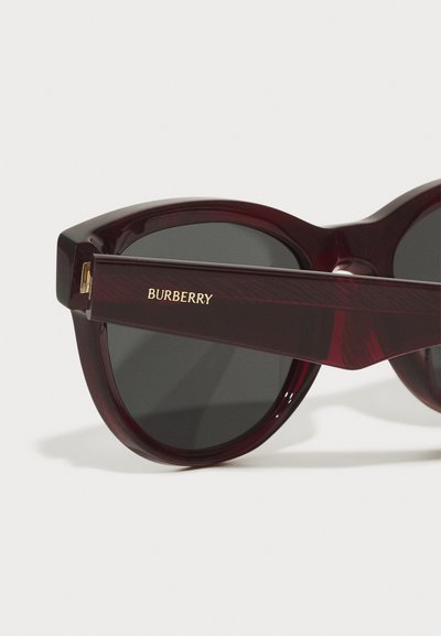 Ümmargused burbooni värvi prillid tumedate objektiivide ja kuldse "Burberry" logo ning templitega. Läikiv viimistlus, paks raami ja nurkse disainiga.