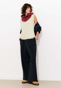 Pull sans manches en crème avec une capuche bordeaux, associé à un pantalon à larges jambes à rayures navy et des mocassins marron.