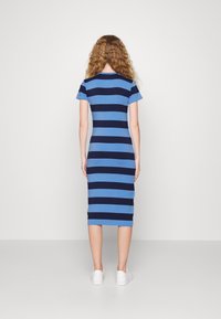 Blå och marinrandig klänning i medellängd med korta ärmar, rundad halsringning och figursydd design. Buren med vita sneakers, minimalistisk stil.