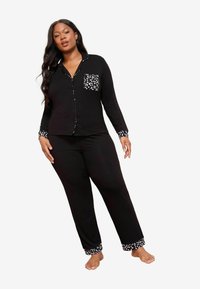 Set de pijama negru format dintr-o bluză cu mânecă lungă, cu nasturi, care are un buzunar cu buline și mansete, asortată cu pantaloni care au accente cu buline.