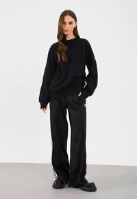 Czarna, oversize'owa bluza zestawiona z czarnymi, zwężanymi sportowymi spodniami z białymi paskami po bokach. Masywne czarne sneakersy na platformie.