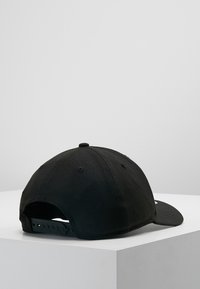 Gorra negra de algodón con visera curvada, cierre ajustable de presión y orificios de ventilación. Color sólido con un detalle mínimo.