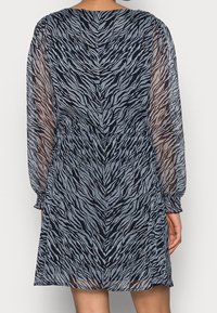 Dlouhé šaty z průsvitné tkaniny s námořnickým a šedým zebrovým vzorem, elastickým pasem a nařasenými manžetami. Texturovaný, volně plynoucí design.