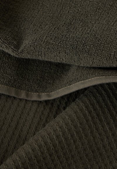 Σκούρο πράσινο υφασμάτινο με υφή, με ραβδώσεις και θηλιές, που παρουσιάζει διπλωμένες στρώσεις και ραμμένα περιθώρια.