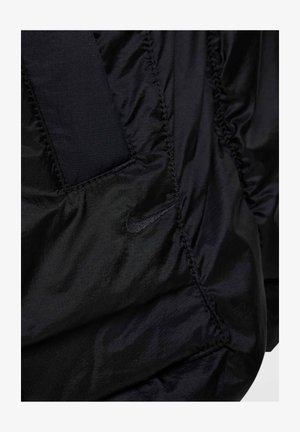 Chaqueta de nylon negra con textura fruncida, costuras horizontales y un pequeño logo de Nike en negro. Cuenta con un acabado suave y brillante.
