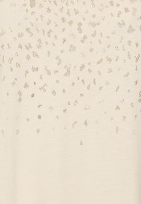 Svetle béžový top s texturovaným vzorem malých, rozptýlených zlatých akcentů, vyrobený z měkké látky a hladké textury.