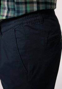 Navyblå, lätta byxor med en slät textur, elastisk midja och sidofickor. Har en bakficka med knapp.