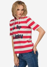 Červeno-bílý pruhovaný krátký rukávové mikina s kapucí, která má na přední straně tmavě modrou grafiku. Vyrobena z měkké tkaniny s uvolněným střihem.