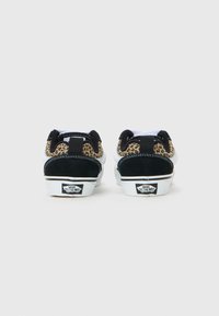 Une paire de baskets Vans basses vues de l'arrière, avec des cols en imprimé léopard, des talons en daim noir, des semelles blanches et des logos "Off The Wall".