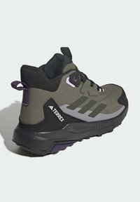 Chaussure de randonnée montante vert olive et noir avec lacets noirs, marque Terrex, avec semelle robuste et languette violette au talon.