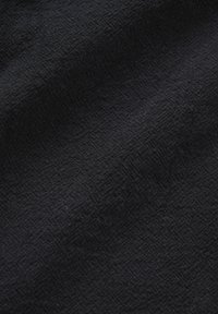 Gros plan sur un tissu noir texturé avec des motifs subtils en forme de losanges et de maille croisée, créant une surface douce et en relief.