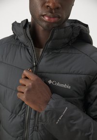 Sort puffjakke med lynlås foran, hætte og "Columbia" logo. Bemærkelsesværdig "Omni-Heat" tekst på ærmet. Glat tekstur.