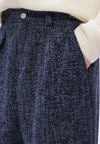 Calças azul-marinho feitas de tecido texturizado com um padrão tecido, apresentando um fecho frontal com botão e bolsos laterais.