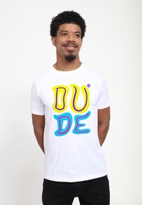 Bílý bavlněný tričko s výrazným, vícebarevným textem "DUDE" v žluté, růžové a modré barvě se hravým, vlnitým písmem. Krátké rukávy.