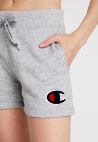 Grå bomullsshorts med en ribbad midja, med sidofickor och en svart och röd broderad logotyp på vänster lår.