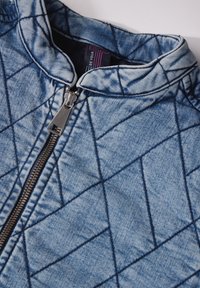 Vuorattu farkkutakki vetoketjulla, jossa on korkea kaulus ja timanttikuosi, vaaleansininen väri tummansinisillä ompeleilla.