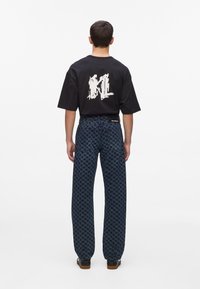 Must mustvalge logo seljal, millele on sobitatud tume sinine houndstooth-mustriga laiad püksid.