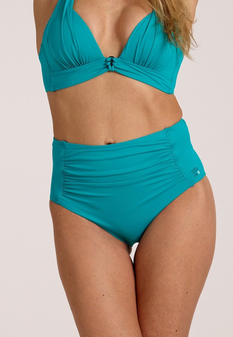 Kvinde iført turkis bikinitrusser med høj talje og matchende bikini top, stående mod en ensartet lys baggrund.