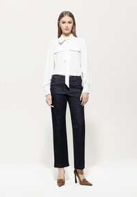 White long-sleeve blouse with a tie-neck detail, paired with dark denim wide-leg pants. Beige stiletto heels complete the outfit.