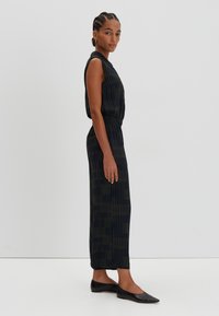 Sleeveless, ankle-length black dress with vertical green stripes, featuring an elastic waistband and a smooth, flowing fabric texture.