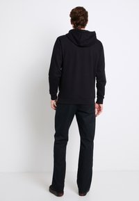 Felpa nera con cappuccio dal texture morbido, polsini e orlo a costine, abbinata a pantaloni scuri. Vista da dietro, che mostra il design della felpa.