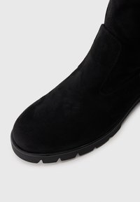 Bottine en daim noir à bout rond avec semelle épaisse en caoutchouc, présentée en angle sur fond blanc.