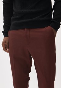 Suéter negro de punto trenzado con un dobladillo acanalado, combinado con pantalones burdeos a medida que presentan una textura suave y bolsillos laterales.