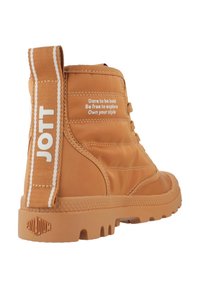 Bottes à cheville beiges avec une semelle en caoutchouc texturée, un haut rembourré et une languette en tissu. Du texte blanc sur le côté présente des phrases motivationnelles.