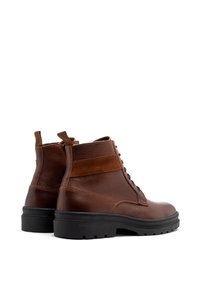 Brązowe skórzane botki sięgające kostki z teksturowanym wykończeniem, zamszowymi akcentami, okrągłym noskiem i czarną gumową podeszwą. Posiadają sznurowane zapięcie z przodu oraz pętelkę do zakładania.