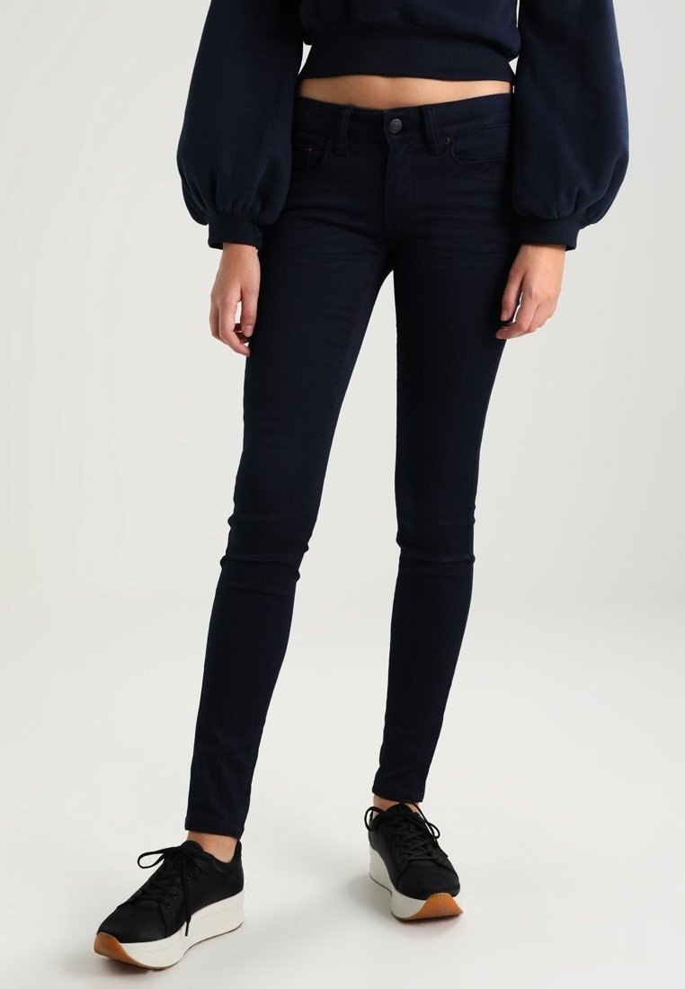 Mörkblå smala jeans i stretchmaterial, med en klassisk femfickdesign och metallknäppning, kombinerat med svarta sneakers.