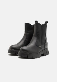 Botas negras de cuero hasta el tobillo con paneles laterales elásticos, suela de goma texturizada y una pestaña trasera para facilitar su uso. Diseño robusto con costuras mínimas.