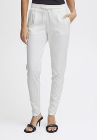 White jogger pants with elastic waistband and drawstring. Features side pockets and a slim fit. Paired with black heeled sandals.