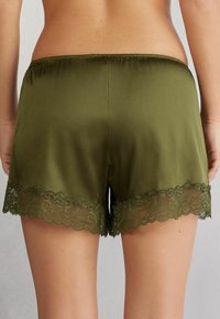 Oliva gröna shorts med en mjuk textur och ett elastiskt midjeband, prydda med en delikat scallop-lace kant i nederkanten.