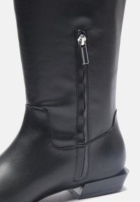 Schwarze Lederstiefel bis zum Knie mit einem eleganten Design, ausgestattet mit einem seitlichen Reißverschluss und einem eckigen Blockabsatz. Glatte Textur mit minimaler Naht.