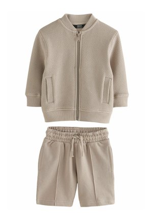 Beige tekstureret lynlåstrøje med ribbede manchetter og kant, kombineret med matchende beige shorts med elastik i taljen og snøre.