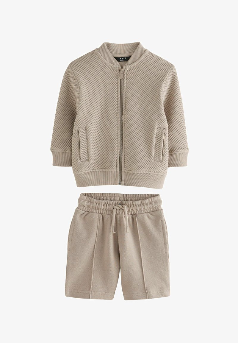 Beige strukturierte Jacke mit Reißverschluss, gerippten Bündchen und Saum, kombiniert mit passenden beigen Shorts mit elastischem Bund und Kordelzug.