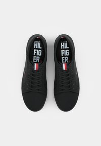 Sneakers nere con una texture liscia, caratterizzate da una chiusura con lacci, suole in gomma e un accento rosso, bianco e blu vicino alla linguetta.