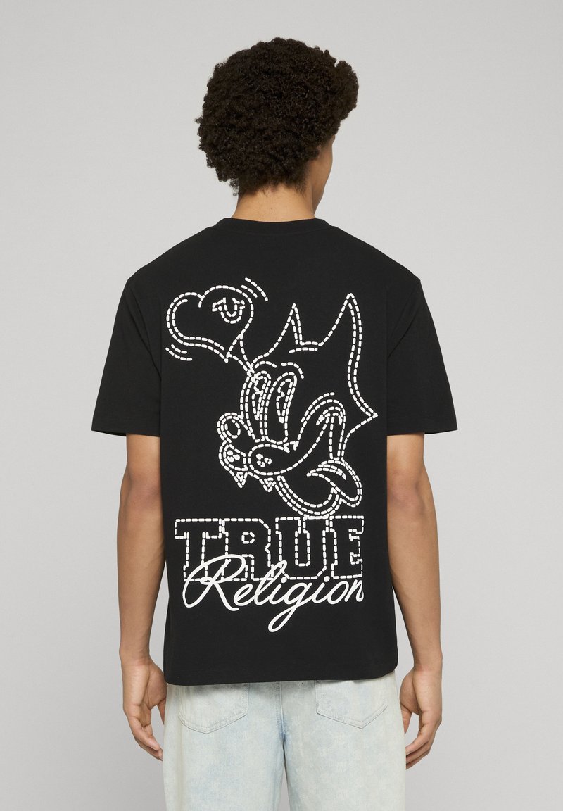 T-shirt in cotone nero con una grande grafica bianca raffigurante un personaggio dei cartoni animati e la scritta "TRUE Religion" sul retro. Design classico con scollo rotondo.