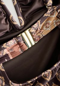 Brauner Stoff-Bikini-Oberteil mit einem floralen Muster in Beige und Rost, mit elastischen Rüschendetails und einem goldfarbenen Verschlussakzent. Die Textiloberfläche ist glatt.