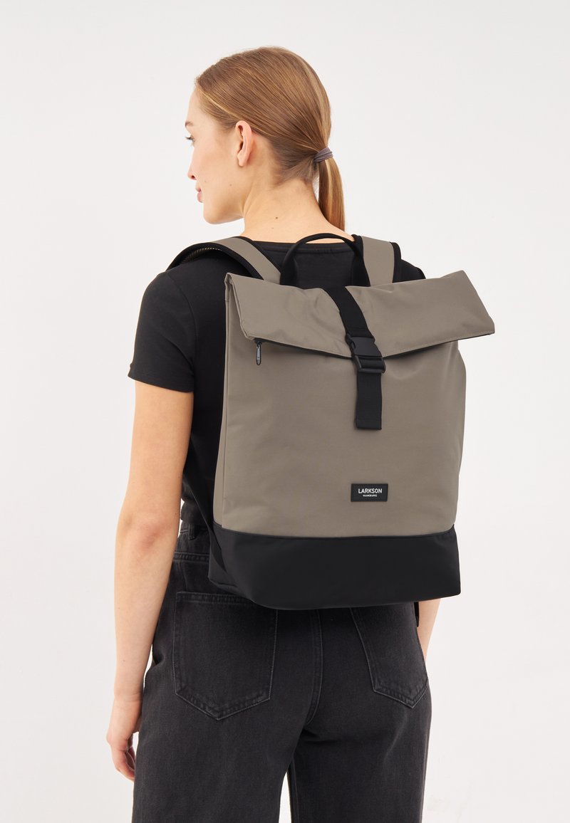 Grå och svart ryggsäck med rulltoppdesign, tillverkad av hållbart tyg. Har en spännesstängning och justerbara remmar för komfort.