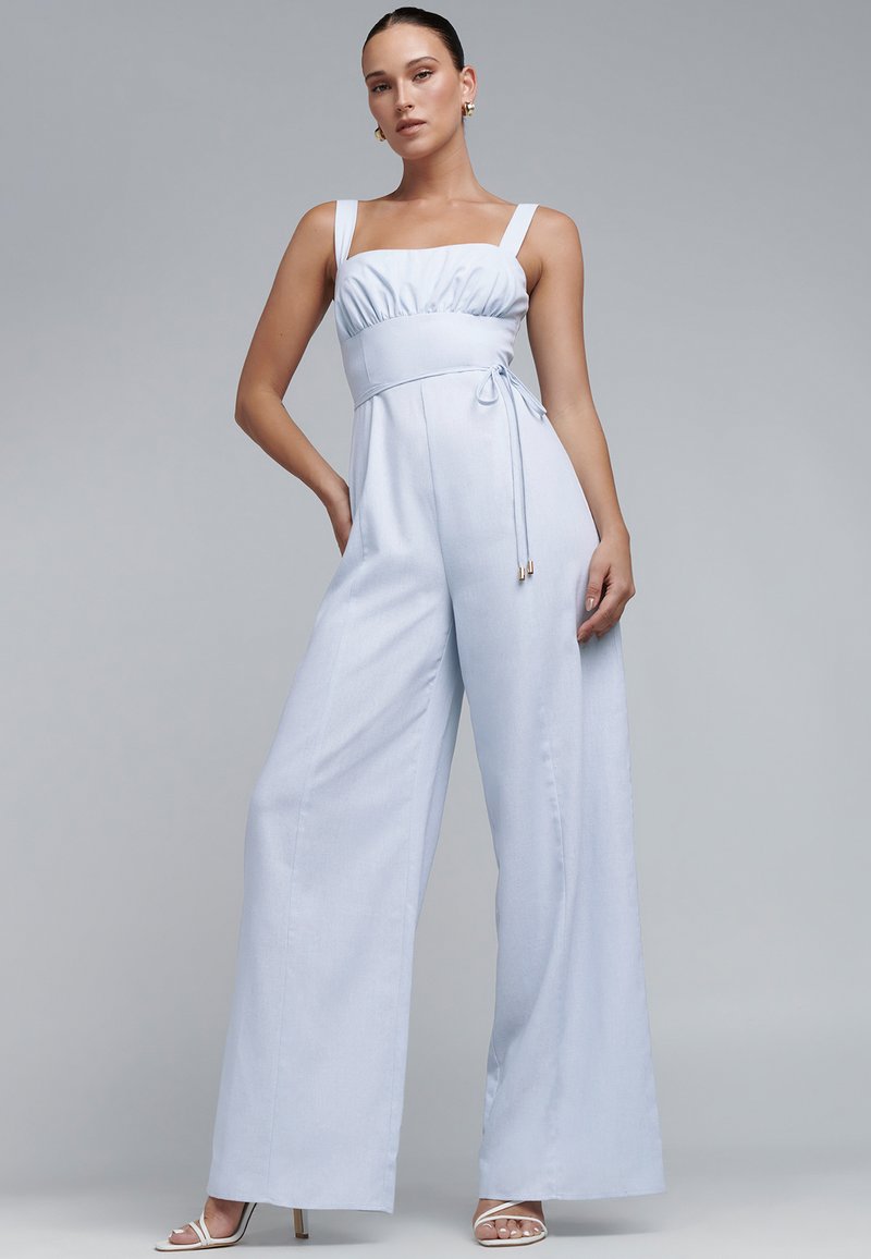 Jasnoniebieski kombinezon z dopasowanym stanem, szerokimi nogawkami i regulowanym wiązaniem w talii. Posiada kwadratowy dekolt i gładką teksturę.