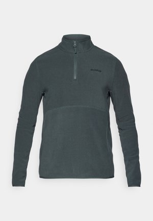 Tamnozeleni polar pulover s polu-zatvaračem, visokim ovratnikom i crnim logotipom na lijevoj strani prsnog koša. Glatka tekstura i prilagođeni dugi rukavi.