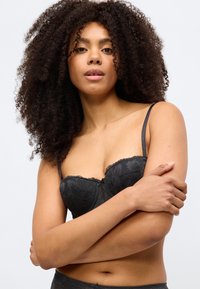 Μαύρο δαντελένιο σουτιέν με ανθικό σχέδιο, κυματιστά άκρα και ρυθμιζόμενα λουριά. Απαλή υφή, ελαφρώς επενδυμένα cups και κεντρική λεπτομέρεια με φιόγκο.