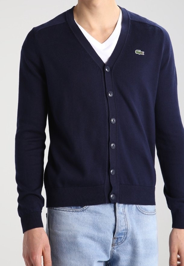 Marinblå cardigan i mjukt stickat tyg, med V-ringning, långa ärmar, framsida med knappar och en liten grön logotyp på bröstet.